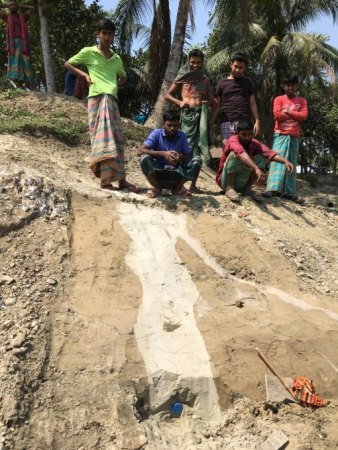 A group of people stand at the top of a steep dirt slope that has a light-colored stripe running down it.